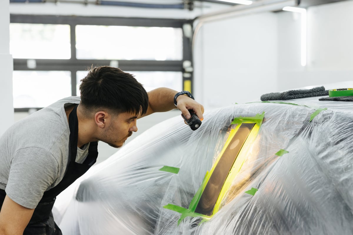 Focused mechanic polishing a restored vehicle panel inside a bright workshop